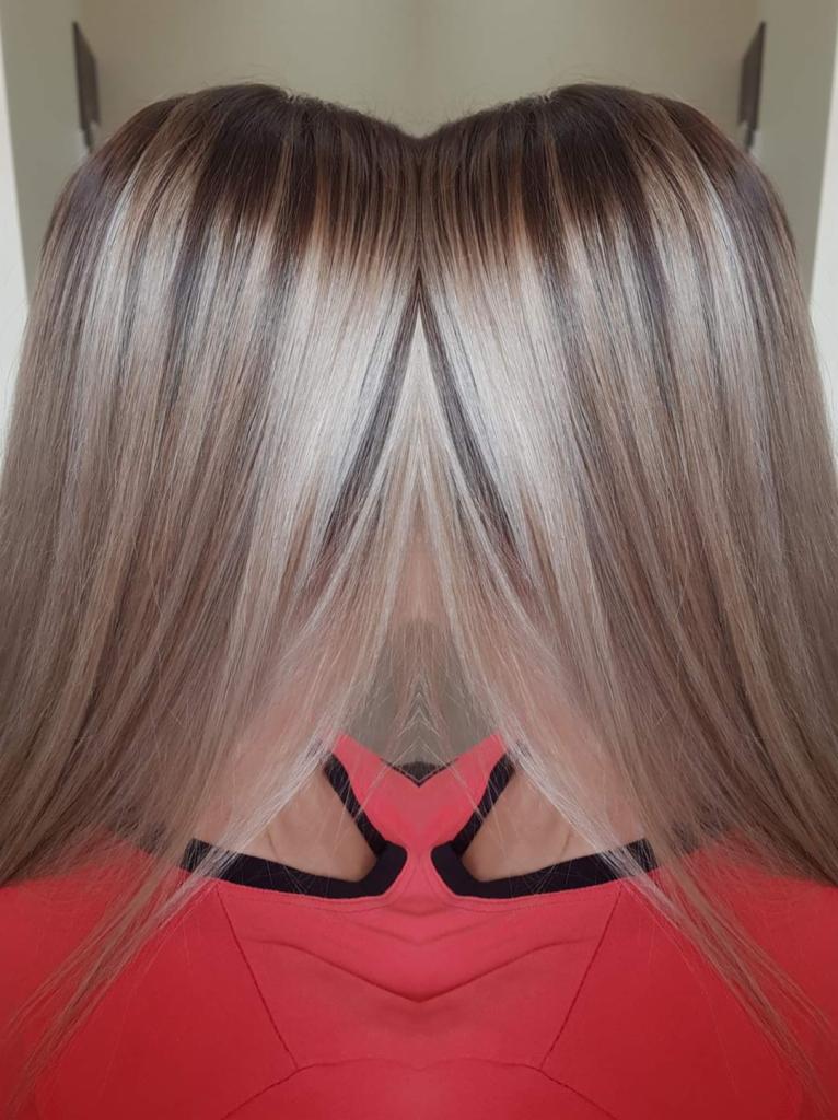Włosy po koloryzacji sombre z widocznymi ciemnymi odrostami i jaśniejszymi pasmami, stylizacja na gładko zaczesana do tyłu.