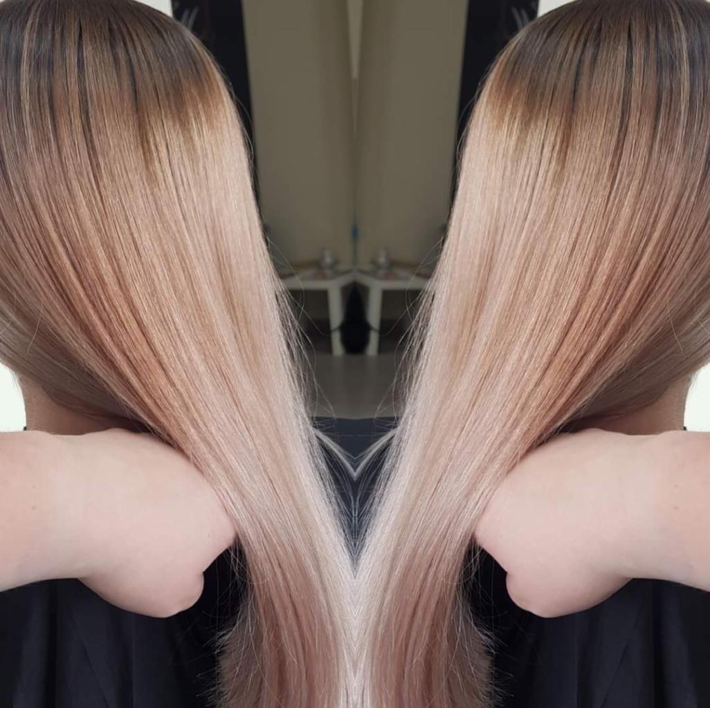 Długie, proste włosy z ombre w odcieniach brązu u nasady i przechodzące w jasny blond na końcach, delikatnie dotykane przez dłonie.