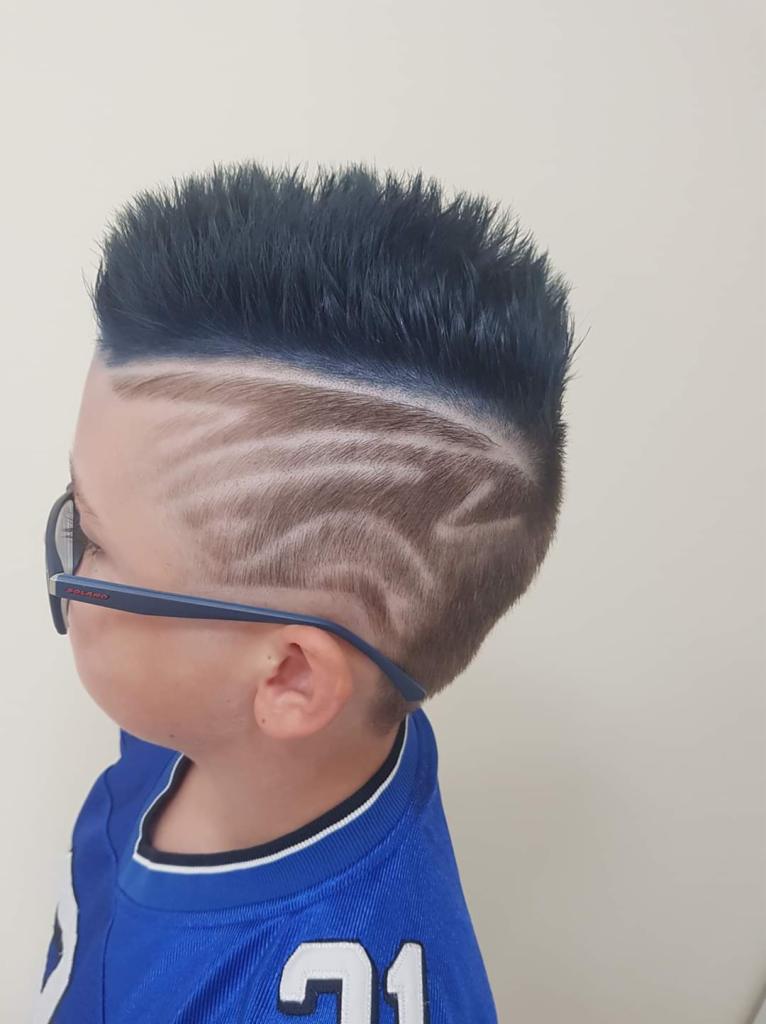 Chłopiec w okularach prezentuje fryzurę z wygolonym wzorem i niebieskimi końcówkami włosów.