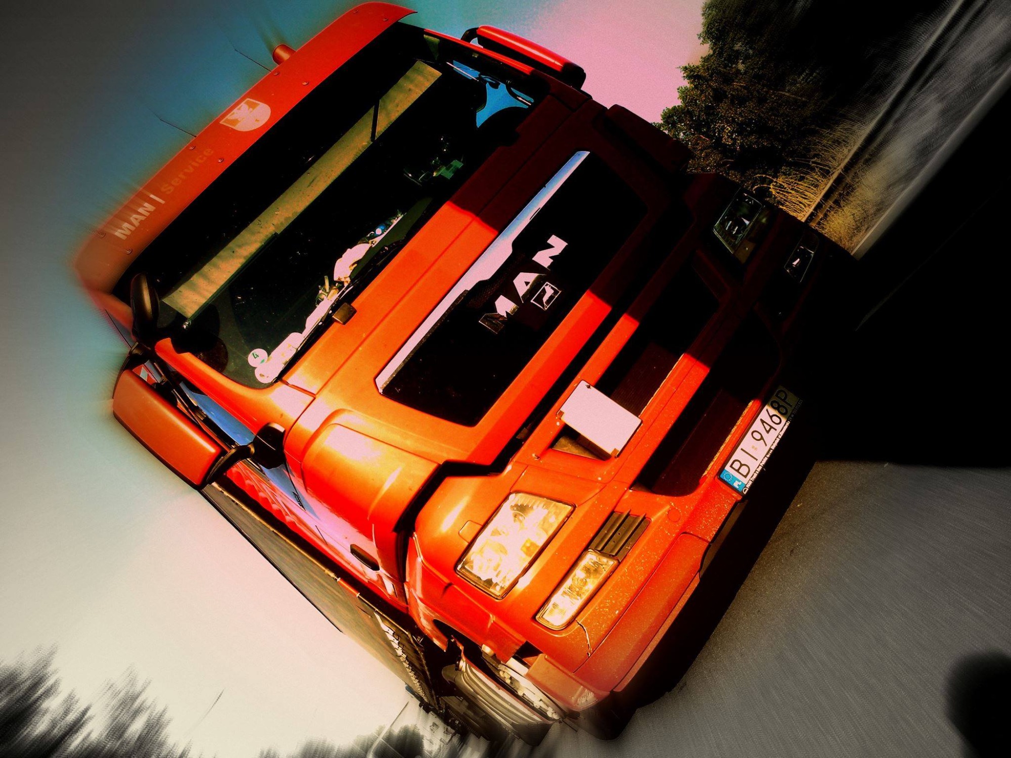 Czerwona ciężarówka marki MAN w ruchu, widoczna z przodu, z numerem rejestracyjnym BI 9468P, z efektem rozmycia ruchu i stylizacją kolorystyczną.