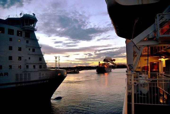 Dwa duże statki w porcie o zmierzchu; jeden z nich z widoczną wieżą kapitańską, drugi z dźwigiem na pokładzie.