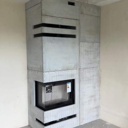 Trzyognie - Nowoczesna obudowa wkładu kominkowego w surowym wykończeniu, widoczna poziomica na podłodze, wnętrze w trakcie wykańczania.