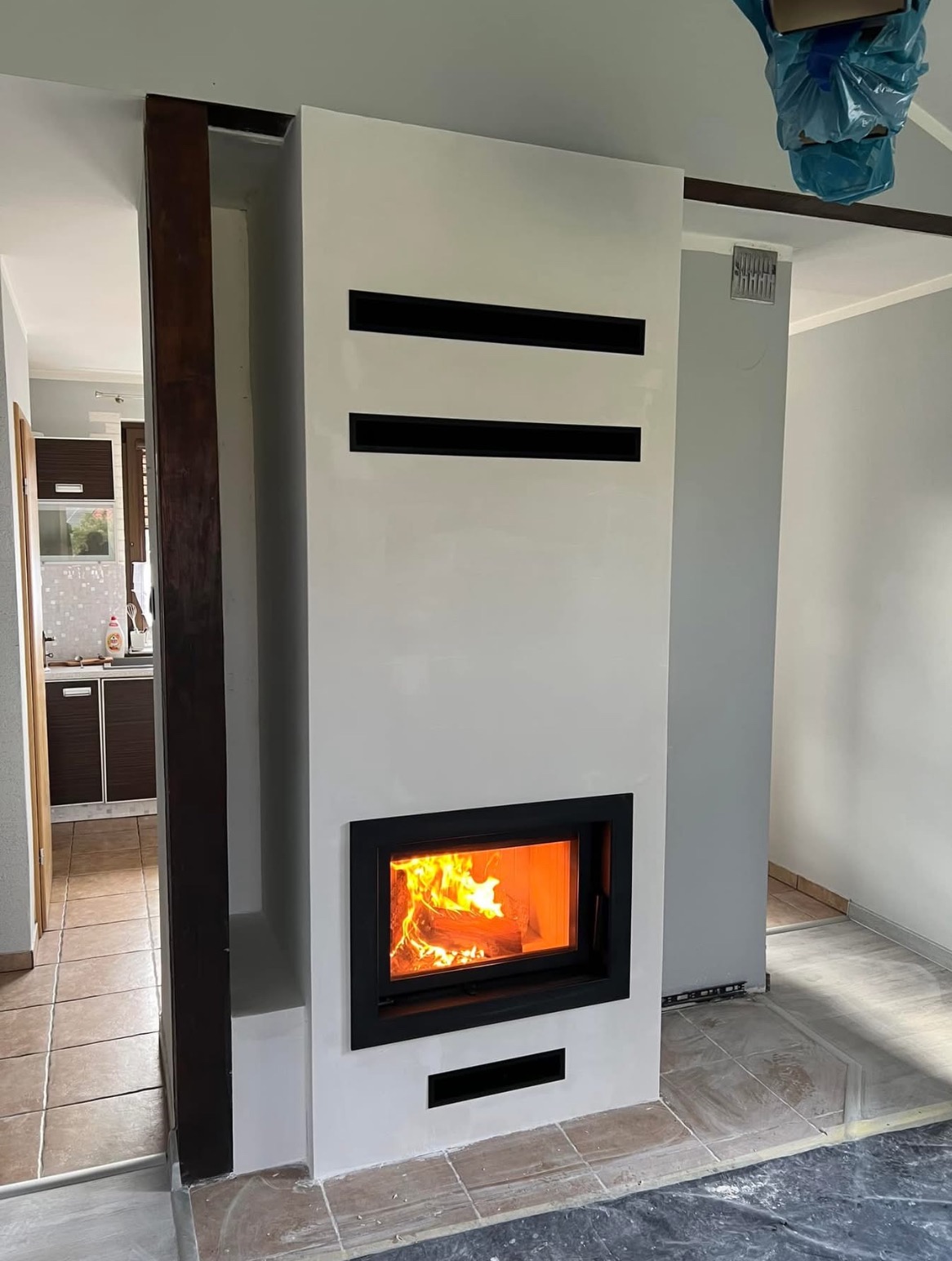 Nowoczesny biały model z czarnymi akcentami i płomieniami, widok na kuchnię w tle, częściowo zakryte podłogi folią ochronną.