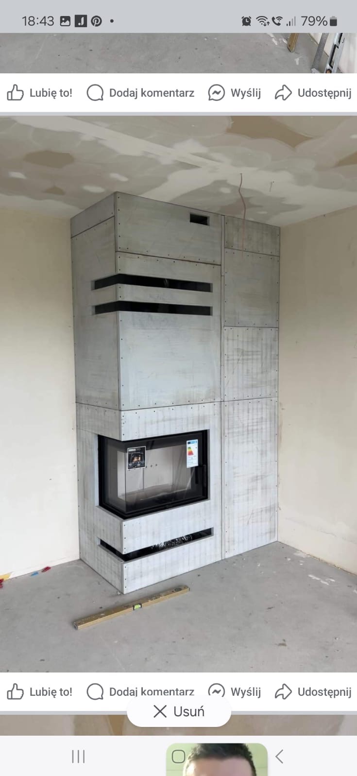 Nowoczesna obudowa wkładu kominkowego w surowym wykończeniu, widoczna poziomica na podłodze, wnętrze w trakcie wykańczania.