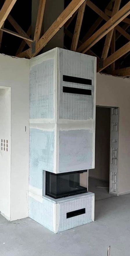 Nowoczesna obudowa wkładu kominkowego w surowym stanie, przed wykończeniem, z widocznymi drewnianymi elementami konstrukcyjnymi stropu.