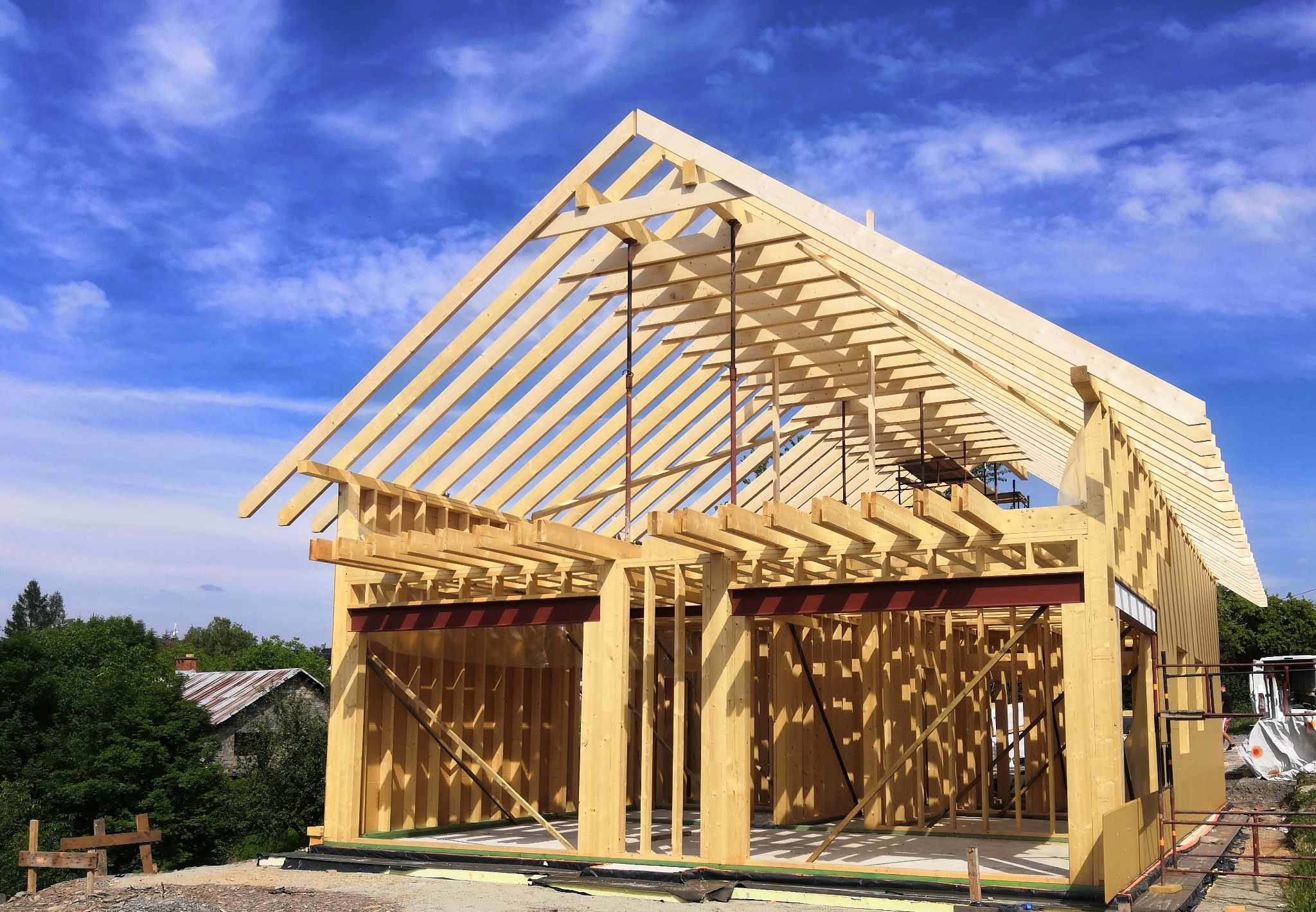 Wznoszenie konstrukcji z drewna klejonego warstwowo, widoczne stalowe belki wzmacniające, błękitne niebo w tle.