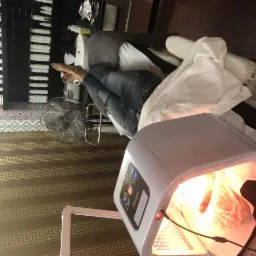 Klientka leży na leżance pod lampą LED w gabinecie, widoczne kosmetyki na półce w tle.