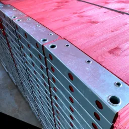 Stos czerwonych, drewnianych płyt szalunkowych z metalowymi wzmocnieniami, spięty taśmą, z widocznym logo SLV Group w lewym dolnym rogu.