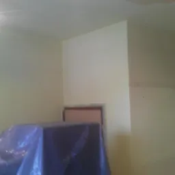 Pokój po malowaniu na jasny odcień, zabezpieczone meble folią, widoczna puszka z farbą.