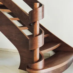 Wolnostojące schody z ciemnego drewna z centralnym słupem i spiralnymi elementami, widok z dołu, minimalistyczny design.
