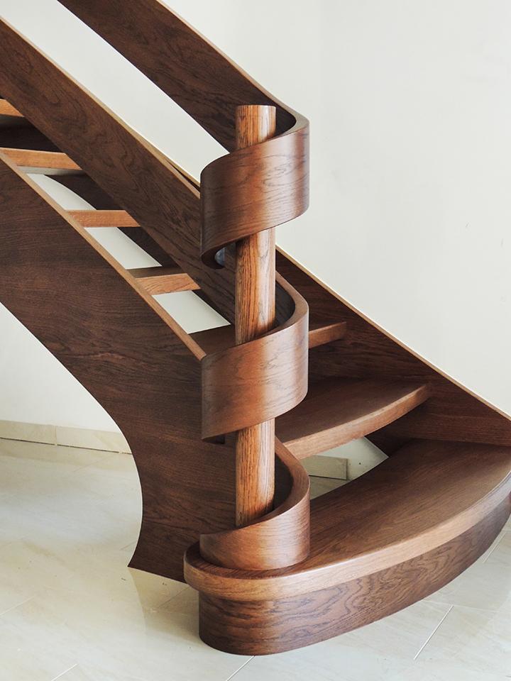 Wolnostojące schody z ciemnego drewna z centralnym słupem i spiralnymi elementami, widok z dołu, minimalistyczny design.