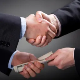 Uścisk dłoni nad plikiem banknotów, szare tło, biznesowe garnitury.