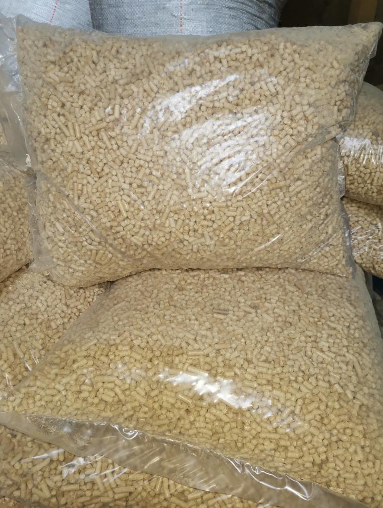 Przezroczyste worki foliowe wypełnione jasnymi, cylindrycznymi granulkami biopaliwa na bazie biomasy, ułożone jeden na drugim.