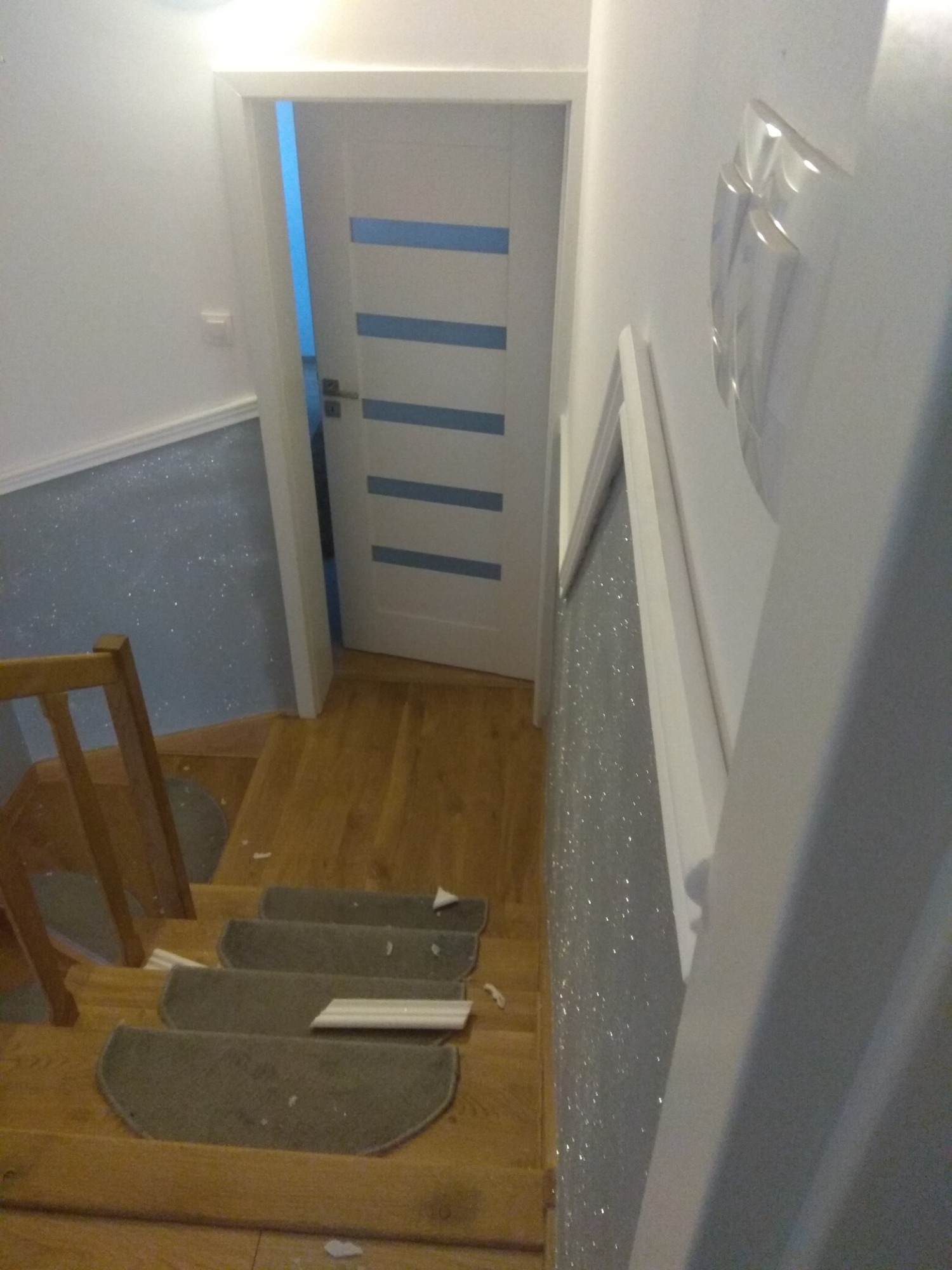 Klatka schodowa w trakcie montażu wykładziny dywanowej na stopniach, widoczne fragmenty listew przypodłogowych i ściana z dekoracyjną fakturą.