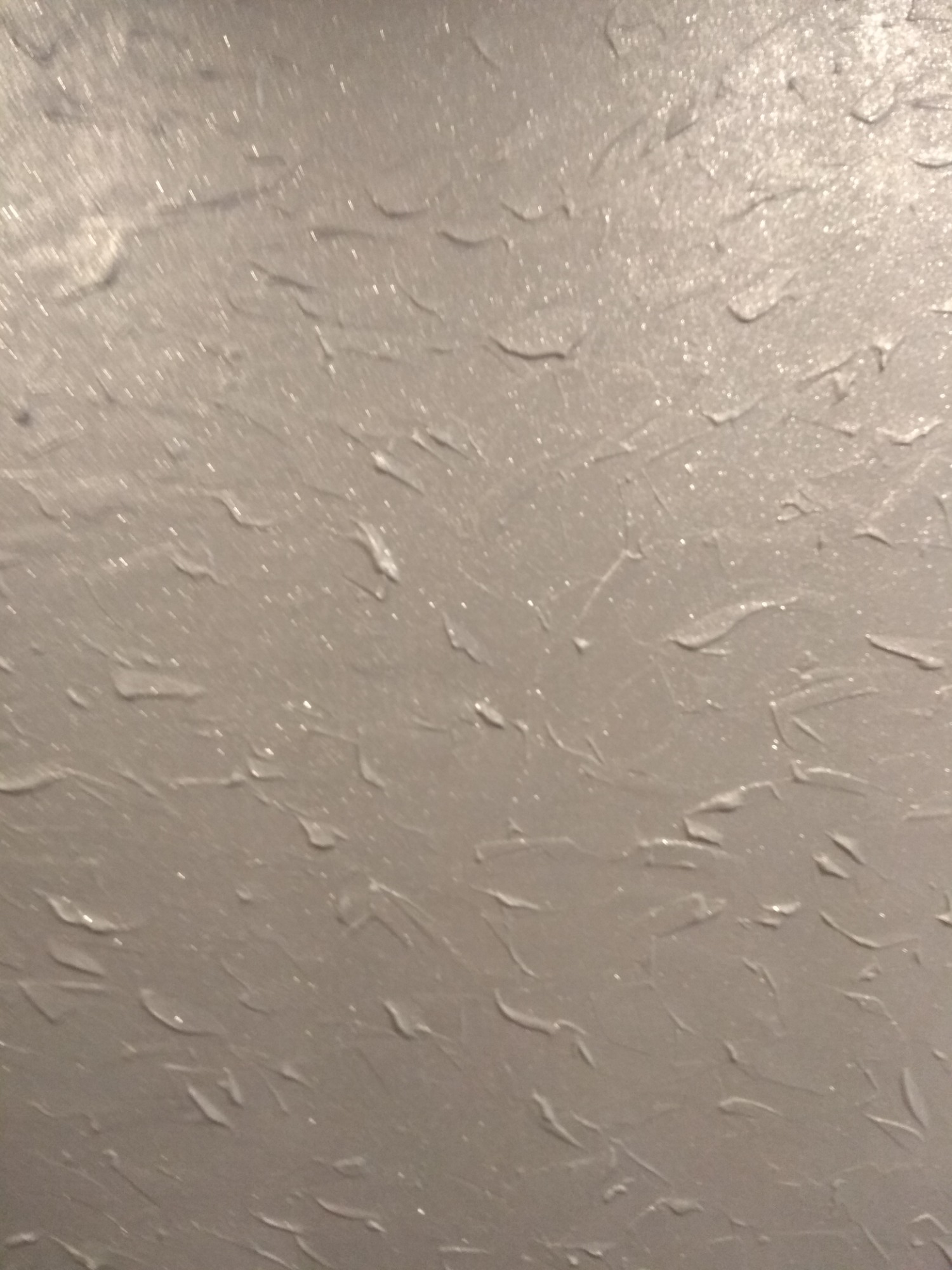 Ściana pokryta szarą farbą strukturalną z delikatnym połyskiem, widoczne ślady pędzla tworzące nieregularny wzór.