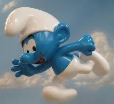 Figurka Smerfa w dynamicznej pozie, biegnącego lub skaczącego, na tle błękitnego nieba z delikatnymi chmurkami.