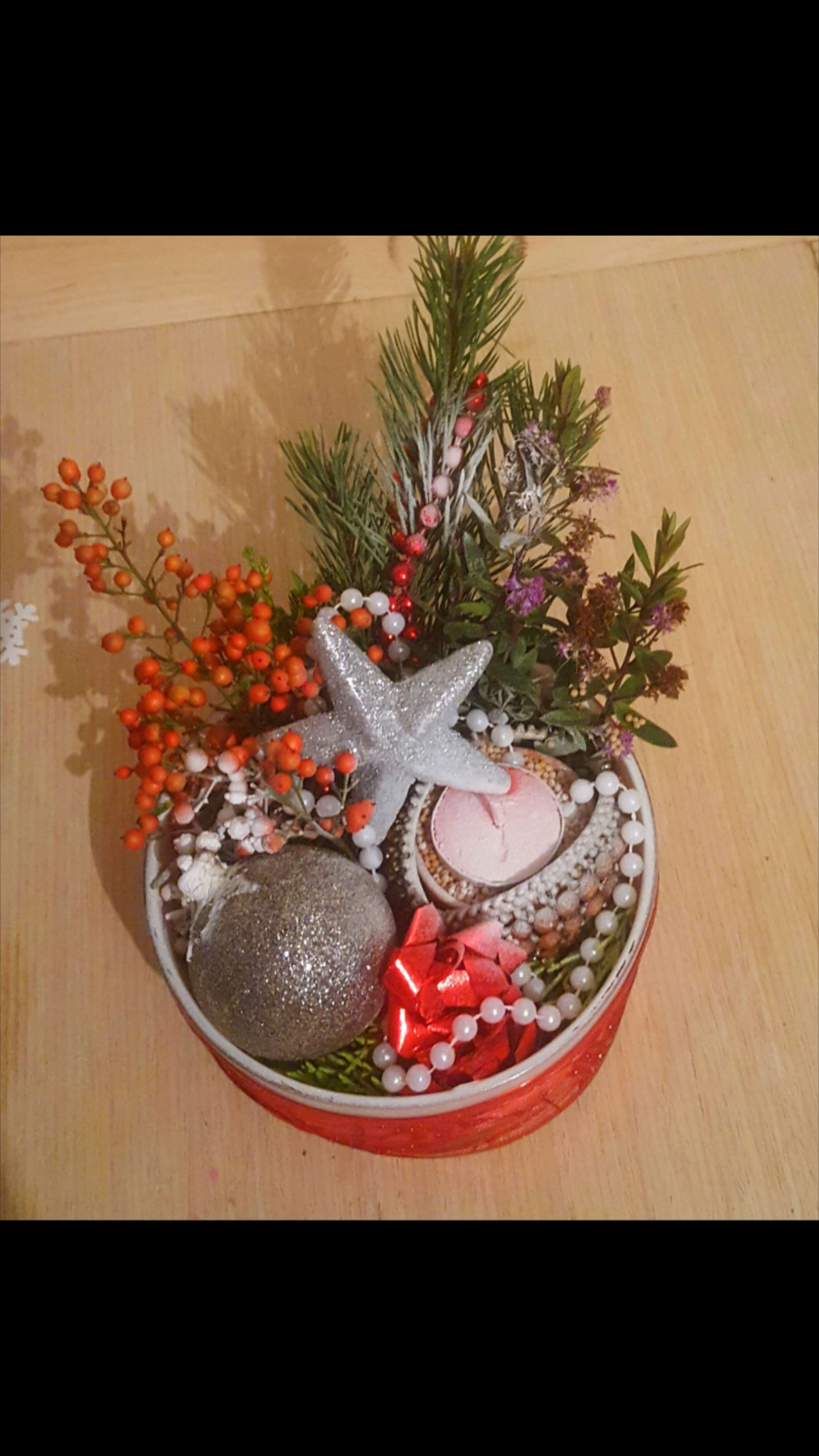 Dekoracja świąteczna w okrągłym, czerwonym pudełku z gałązkami świerku, srebrną gwiazdą, bombką, czerwonym kokardką, białymi koralikami i jarzębiną na drewnianym tle.