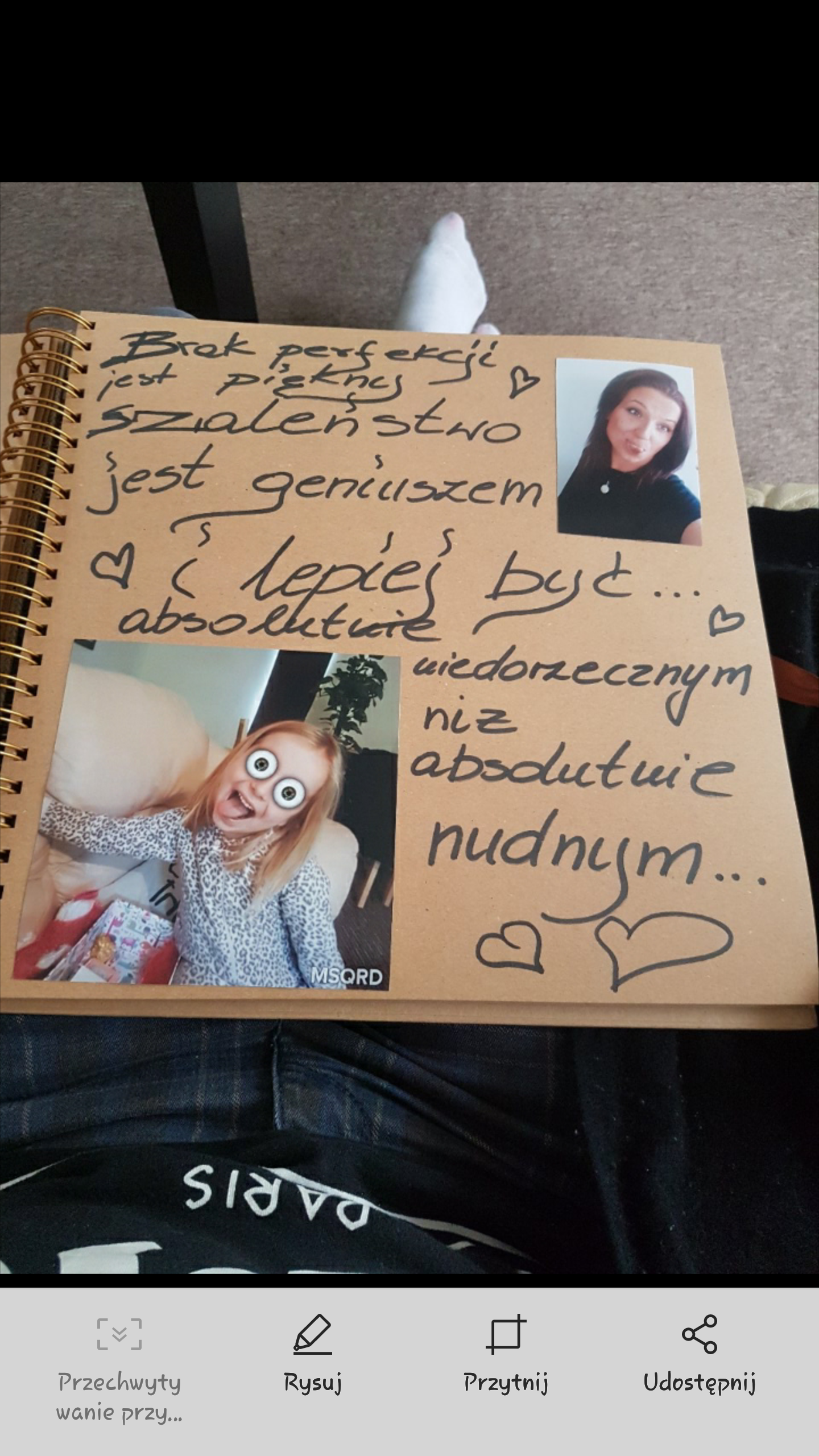 Otwarty brązowy notes spiralny z odręcznym napisem 'Brak perfekcji jest pięknem, szaleństwo jest geniuszem i lepiej być absolutnie niedorzecznym niż absolutnie nudnym...' oraz naklejonymi zdjęciami...