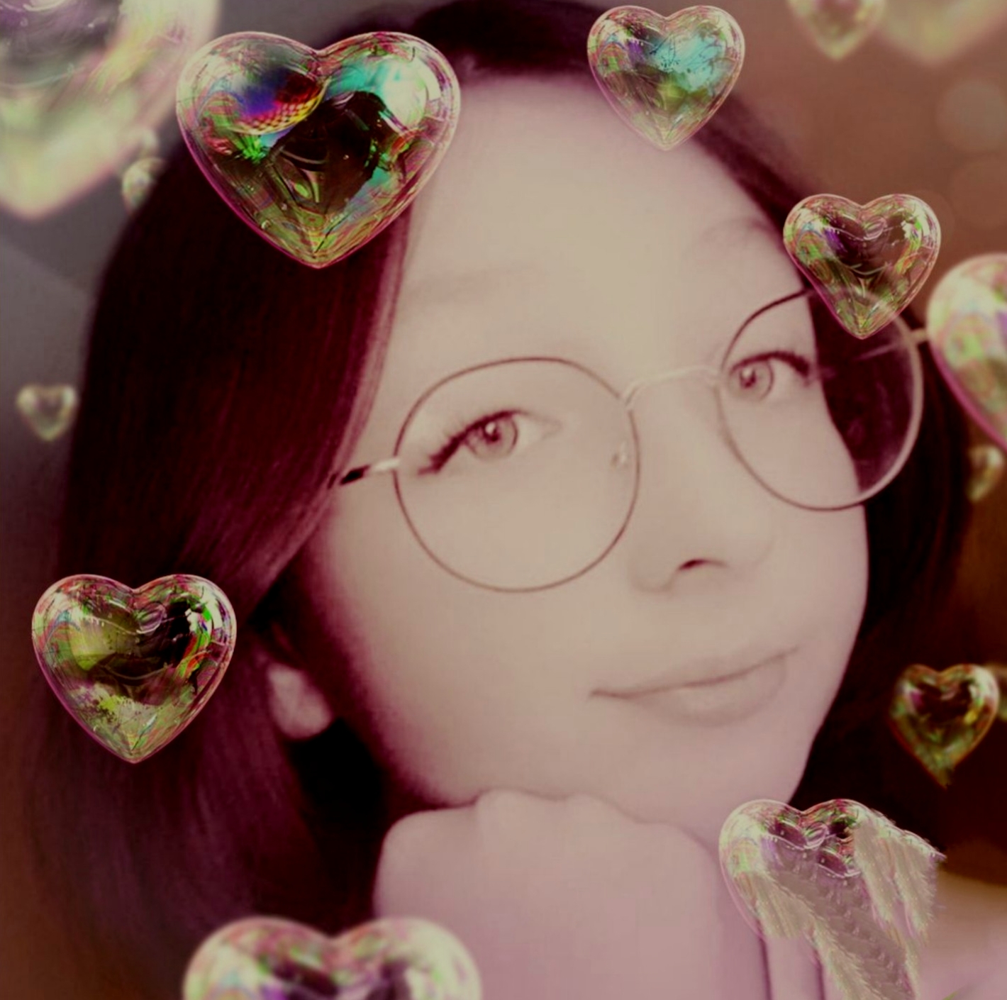 Portret kobiety w okularach otoczonej przez serca w kształcie bąbelków mydlanych z tęczowymi refleksami, na rozmytym tle.