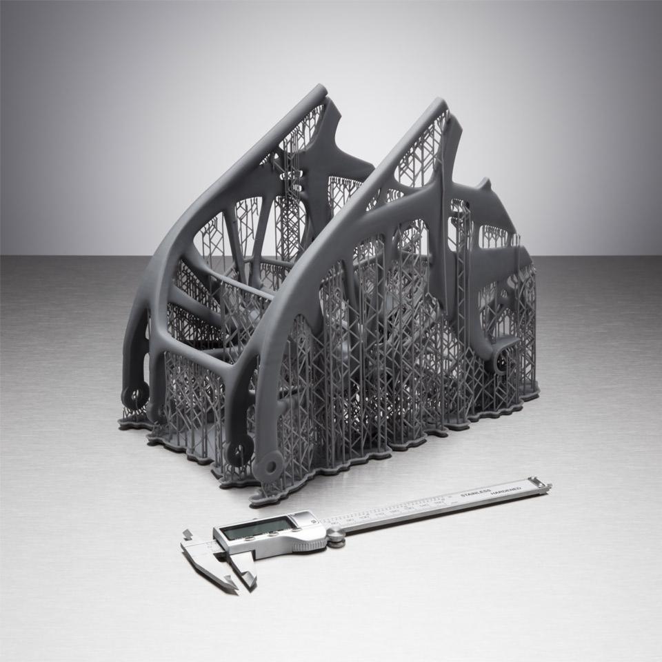 Szary, ażurowy model konstrukcyjny z podpórkami, wydrukowany w 3D, leżący obok suwmiarki elektronicznej na metalowej powierzchni.