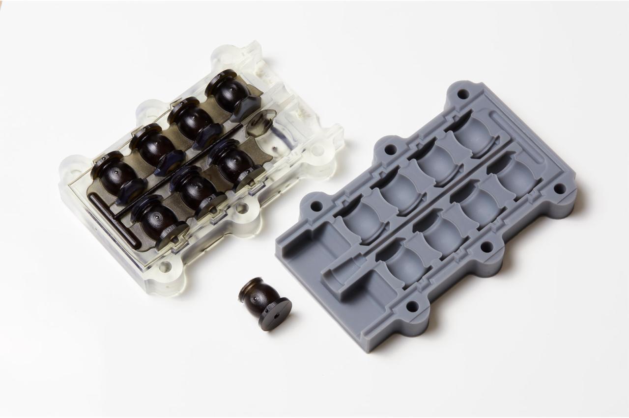 Dwie części formy wtryskowej: przezroczysta z czarnymi elementami wewnątrz i szara pusta, obok pojedynczy czarny element na białym tle.