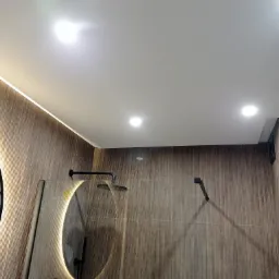 Nowoczesna kabina prysznicowa z deszczownicą, podświetlanym lustrem i ścianami wyłożonymi panelami imitującymi drewno.