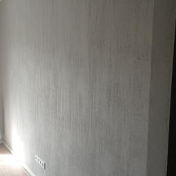 REMVIK - Szara ściana z fakturą, listwa przypodłogowa i gniazdka elektryczne, fragment drewnianej podłogi, widok z dołu.