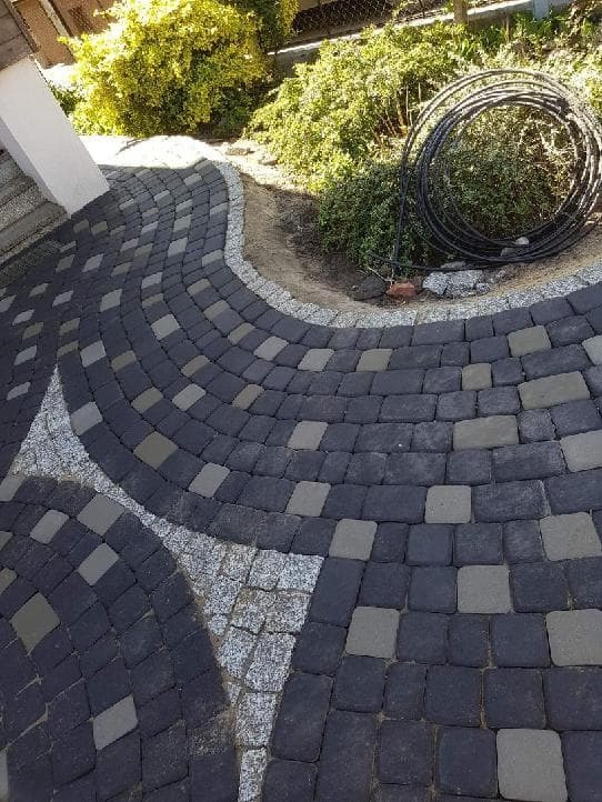 Ułożona kostka brukowa w Gołańczu, wzór z ciemnych i jasnych kostek, obrzeże z drobnego kamienia, zwinięty wąż ogrodowy leży obok.