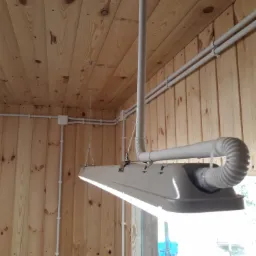 Wnętrze wykończone drewnem z widoczną lampą LED zawieszoną na metalowych linkach oraz białymi przewodami elektrycznymi biegnącymi po ścianach i suficie.