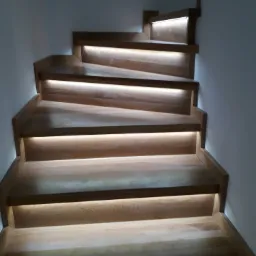 Drewniane schody z subtelnym oświetleniem LED pod każdym stopniem, tworzące ciepłą atmosferę w nowoczesnym wnętrzu.