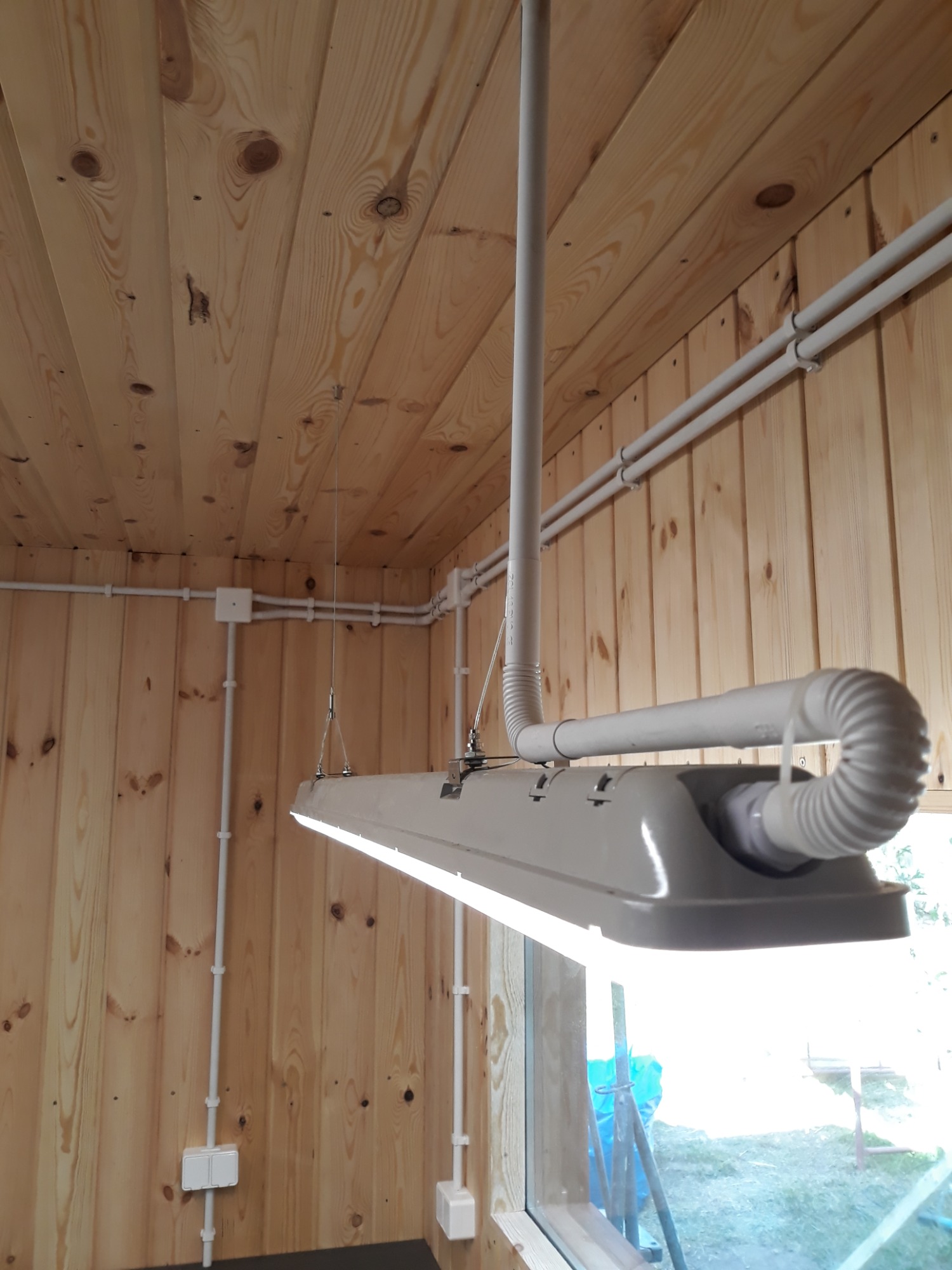 Wnętrze wykończone drewnem z widoczną lampą LED zawieszoną na metalowych linkach oraz białymi przewodami elektrycznymi biegnącymi po ścianach i suficie.