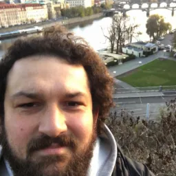 Mężczyzna z brodą robi selfie na tle Wełtawy i mostów w Pradze. Nietypowy kadr z podróży. Fotografia wykonana we Wrocławiu.
