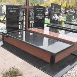 Częściowo polerowany, czarny granitowy nagrobek z elementami z czerwonego granitu, z wyrytymi wizerunkami religijnymi i inskrypcjami, ustawiony na cmentarzu z innymi nagrobkami w tle.