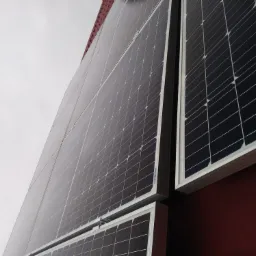 Panel słoneczny na dachu z widoczną strukturą krzemową i białą ramą, uchwycony pod kątem z pochmurnym niebem w tle.