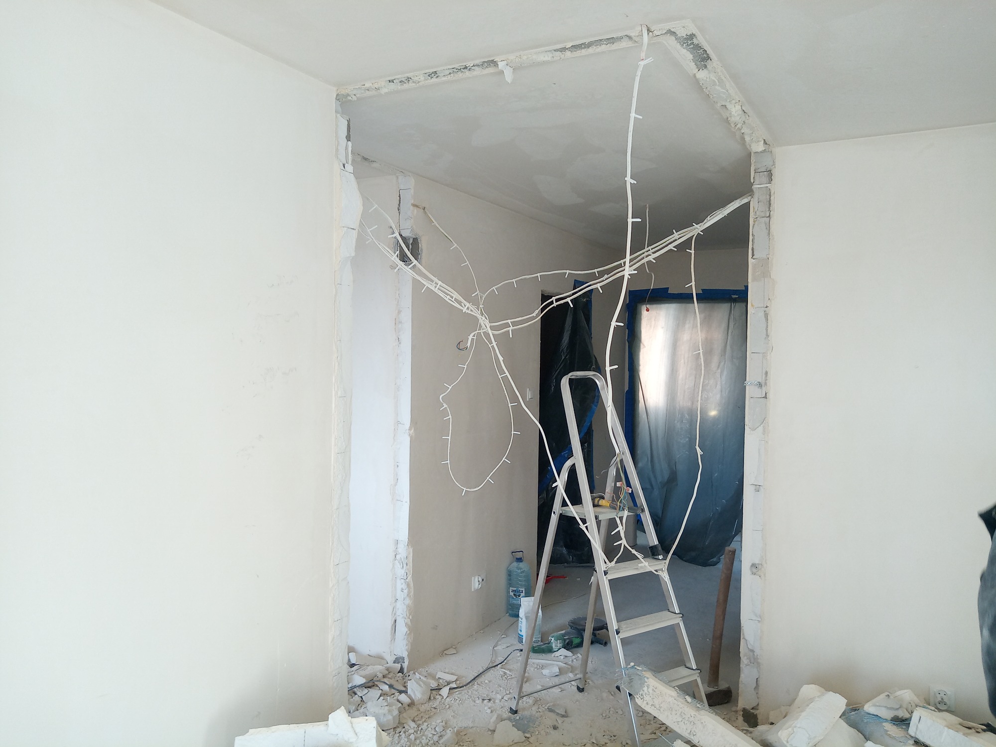 Demontaż ściany i instalacja elektryczna w trakcie remontu, widoczne przewody, gruz i drabina aluminiowa