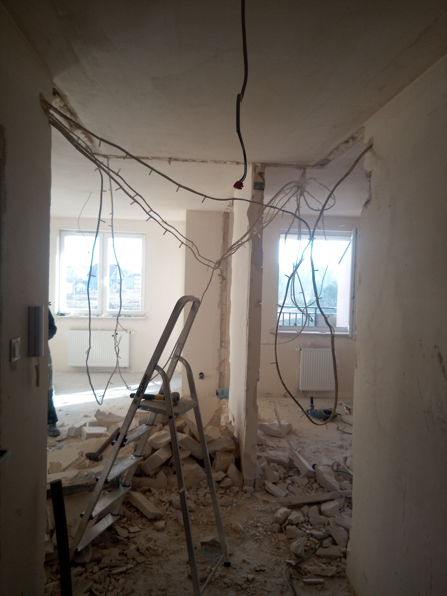 Demontaż ścian działowych w mieszkaniu, widoczne gruz, wystające przewody elektryczne i drabina aluminiowa.