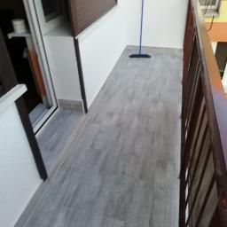 Sebastian Grabski - Wykończony balkon z szarymi płytkami imitującymi drewno, brązowa balustrada i niebieski mop w rogu, widok z góry.