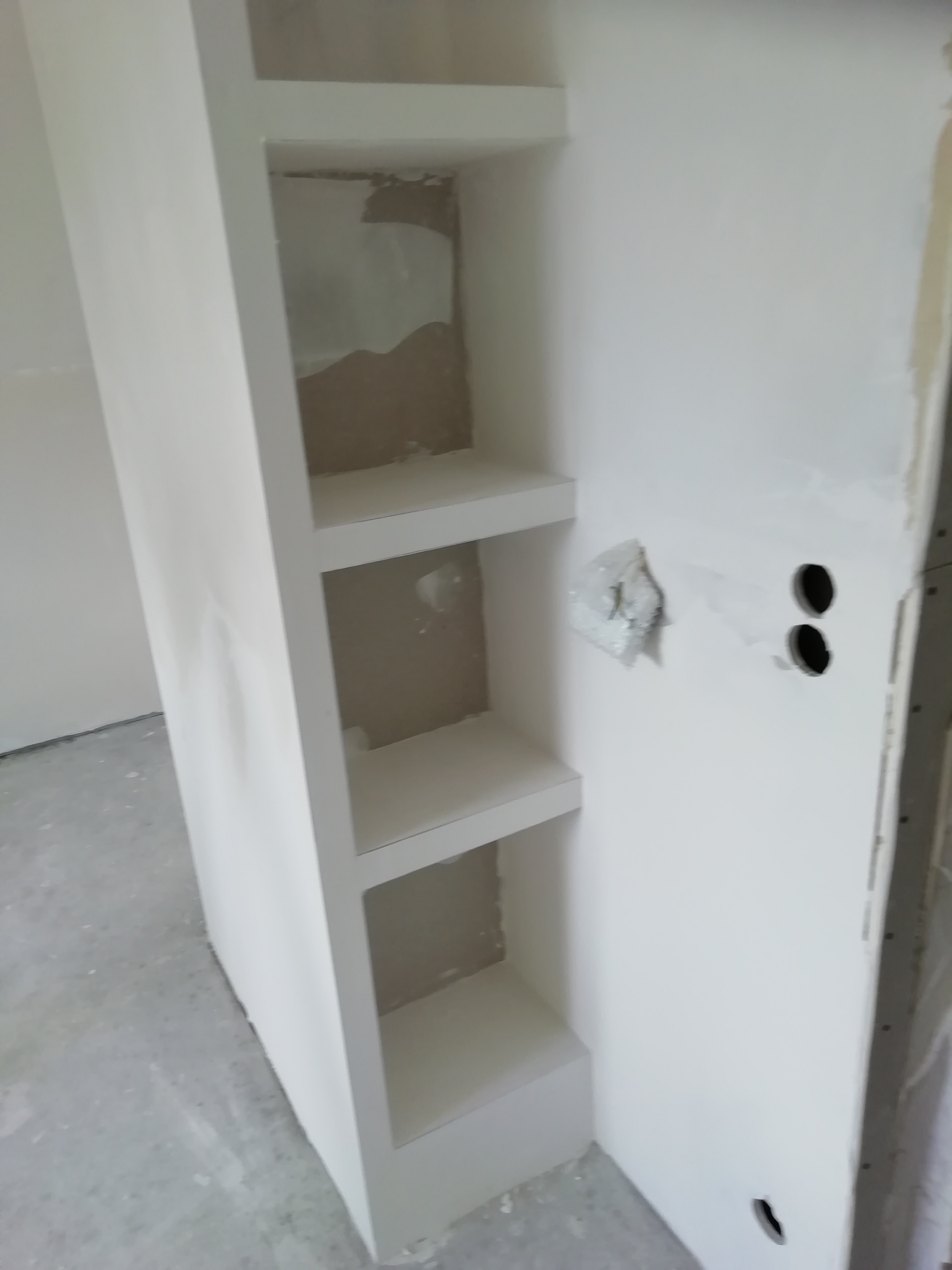 Narożna wnęka z półkami z płyty karton gips, przed malowaniem, widoczne otwory na gniazdka elektryczne i niedoskonałości szpachlowania.