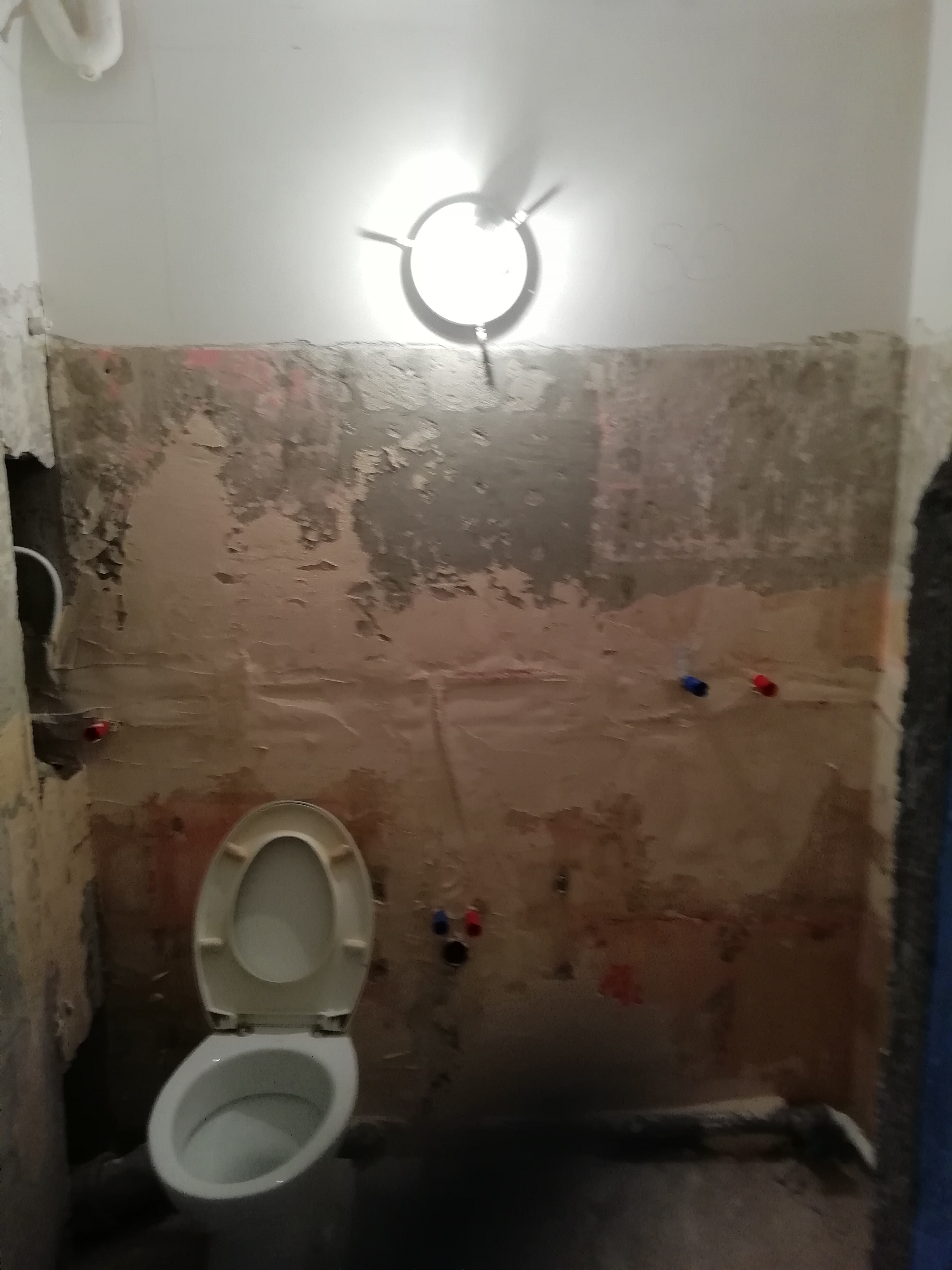 Łazienka w Bydgoszczy w trakcie demontażu starej glazury i przygotowania do położenia nowych płytek, widoczne odsłonięte ściany, instalacja wodna i toaleta z otwartą klapą.