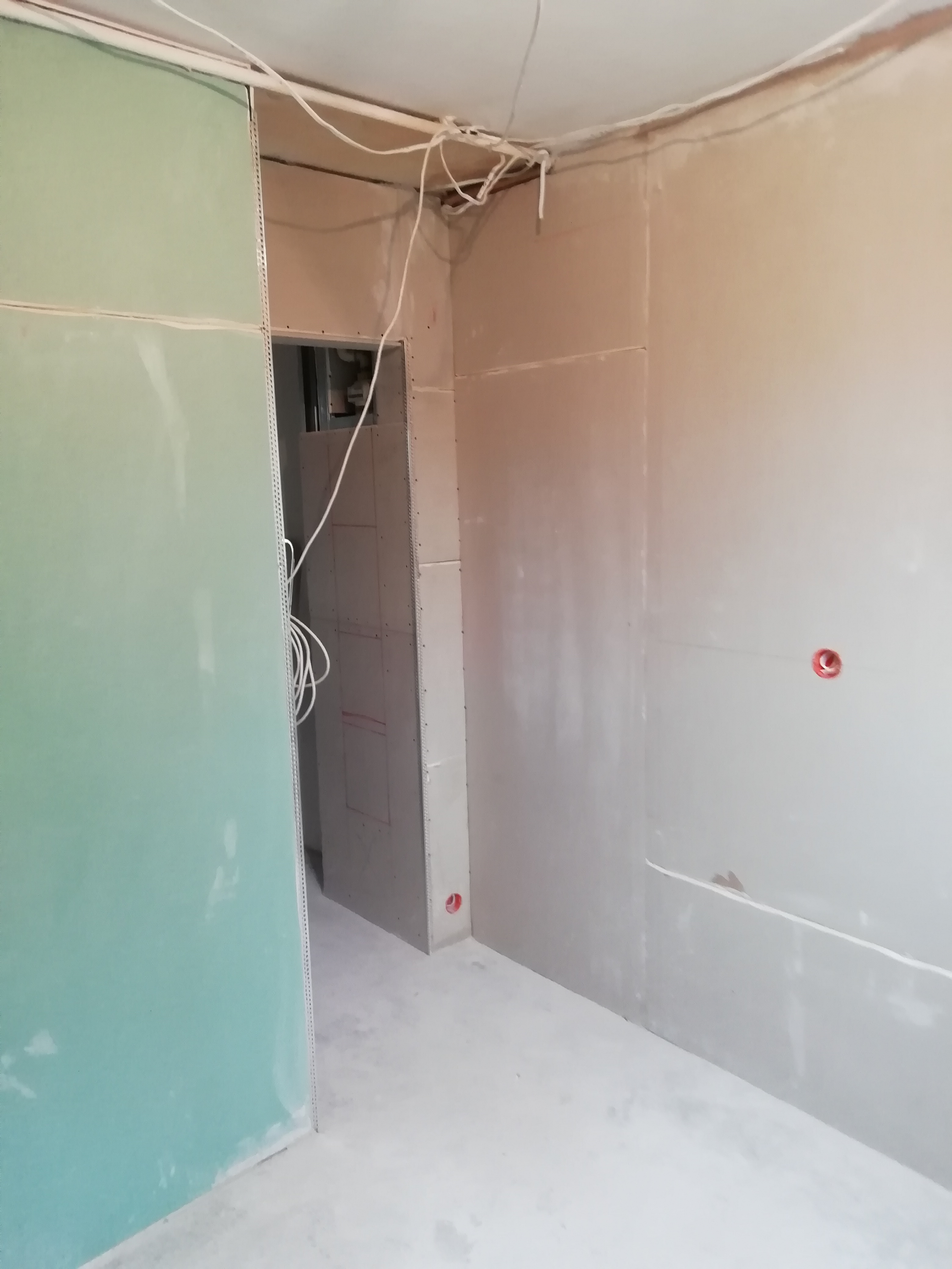 Wnętrze w trakcie montażu płyt kartonowo-gipsowych z widocznymi przewodami elektrycznymi na suficie i metalowymi narożnikami zabezpieczającymi krawędzie.