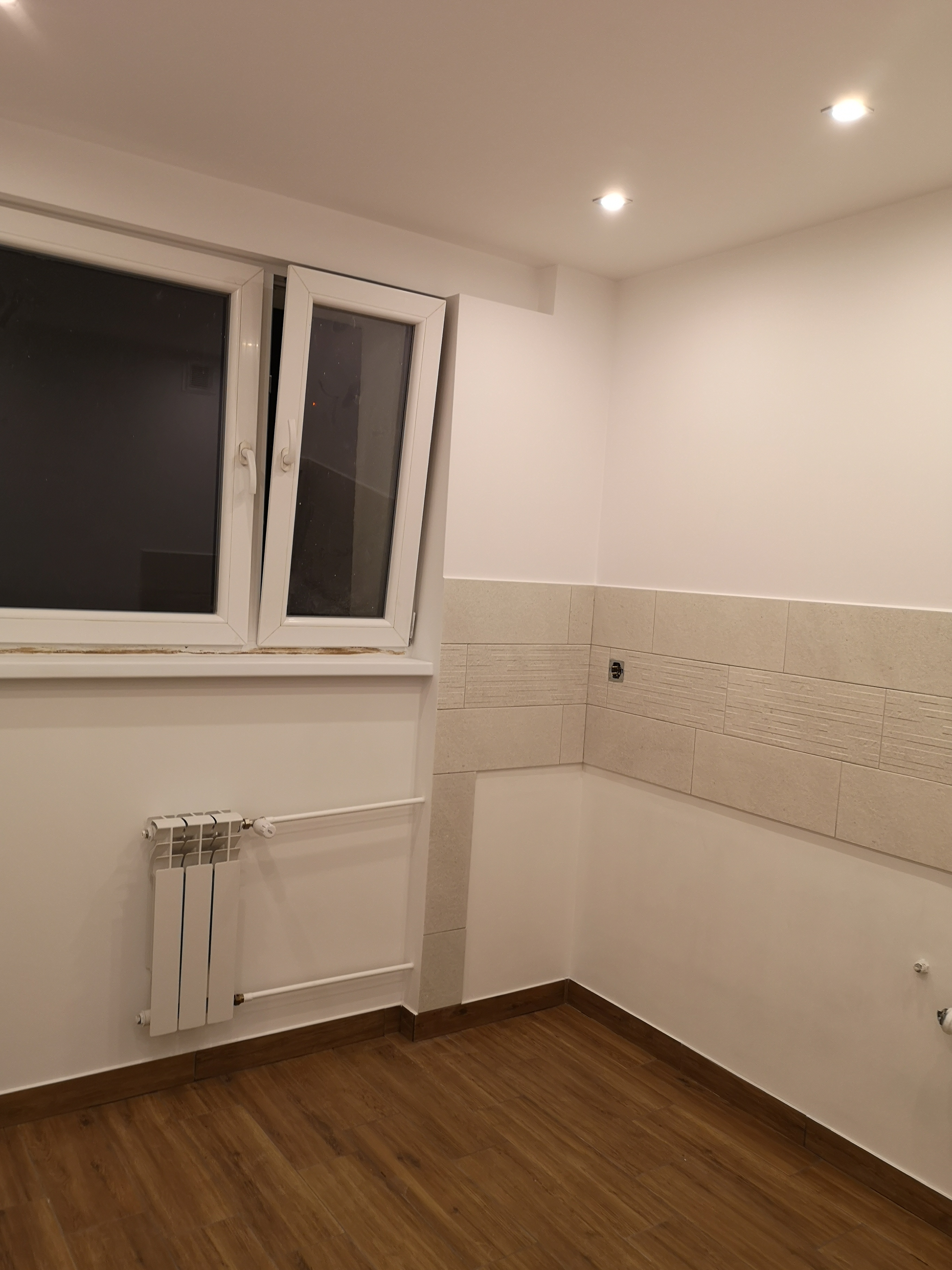 Wykończona łazienka z beżowymi płytkami imitującymi kamień, drewnopodobną podłogą, białym grzejnikiem i otwartym oknem.