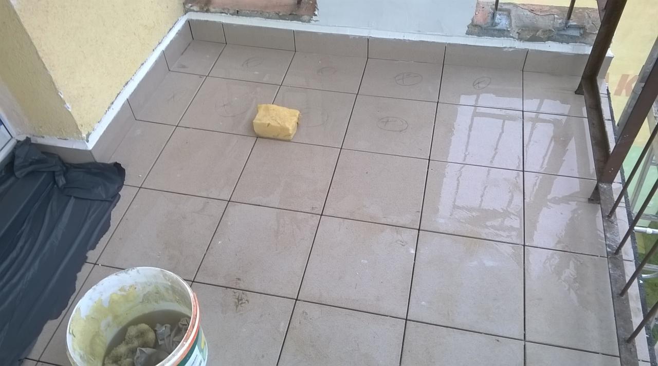 Balkon w trakcie układania płytek, widoczna gąbka, wiadro z wodą i zarysowane miejsca na płytki.