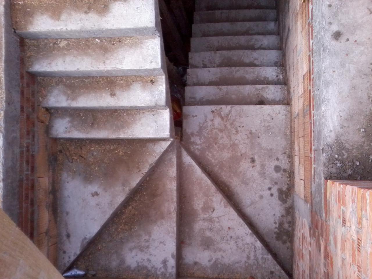 Surowe betonowe schody w trakcie budowy, widoczne ślady zaprawy i cegieł na ścianach bocznych, oświetlenie naturalne podkreśla szorstką fakturę betonu.