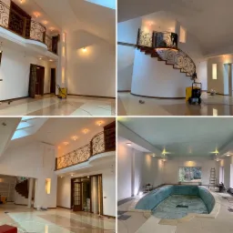 Przestronne wnętrze domu z galerią, schodami i basenem po malowaniu, widoczne detale wykończenia ścian i podłóg, żółty osuszacz budowlany w rogu pomieszczenia.