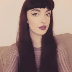 Portret kobiety z ciemnymi włosami, mocnym makijażem ust w odcieniu fuksji i wyraźną kreską na powiekach. Widoczny piercing w nosie i bluzka w paski.