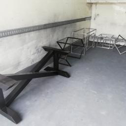 Usługi spawalnicze obrubka metali Pw-spaw - Metalowe konstrukcje w surowym wnętrzu, czarna podstawa stołu na pierwszym planie, za nią srebrne ramy w kształcie sześcianów i trójkątów, widoczne ślady po spawaniu.