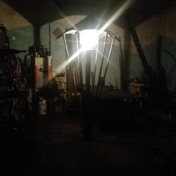 Usługi spawalnicze obrubka metali Pw-spaw - Wnętrze warsztatu ślusarskiego w słabym oświetleniu, z widoczną konstrukcją metalową przypominającą lampę uliczną w trakcie tworzenia.