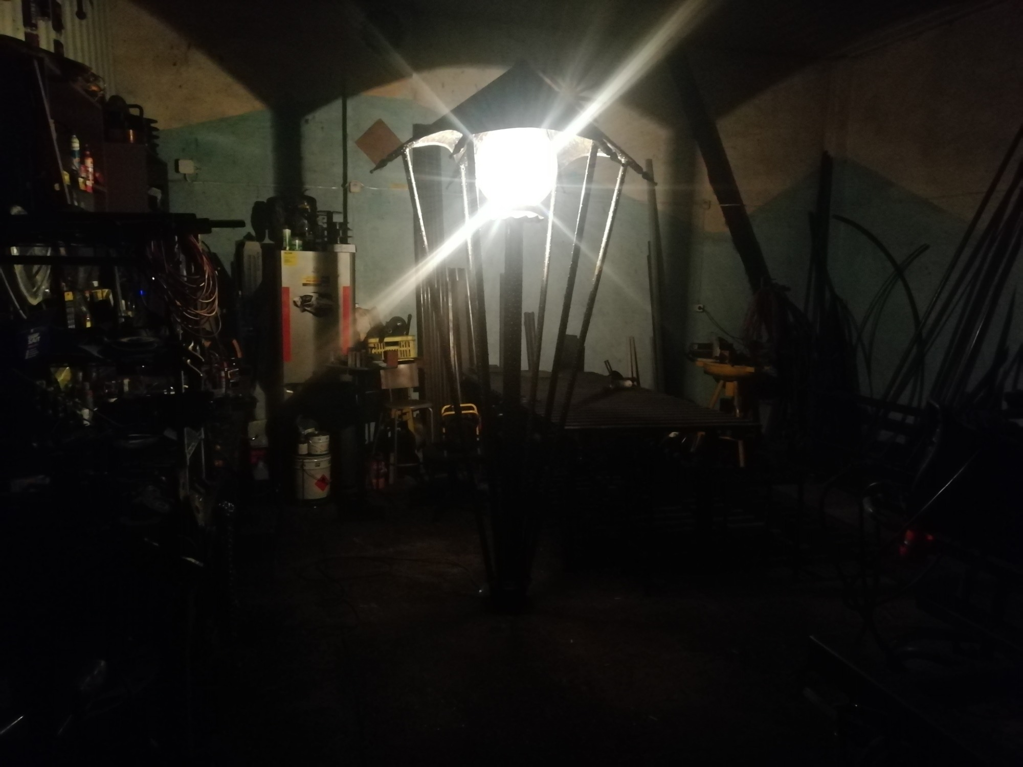 Wnętrze warsztatu ślusarskiego w słabym oświetleniu, z widoczną konstrukcją metalową przypominającą lampę uliczną w trakcie tworzenia.
