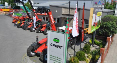 Rząd czerwonych maszyn budowlanych, w tym teleskopowych, przed budynkiem firmy Gravit z widocznym logo i tablicą reklamową.