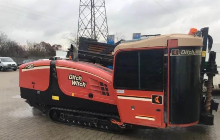 Pomarańczowo-czarna maszyna do przewiertów sterowanych marki Ditch Witch JT30 na gąsienicach, widoczna z boku na tle betonowej nawierzchni i słupa wysokiego napięcia.